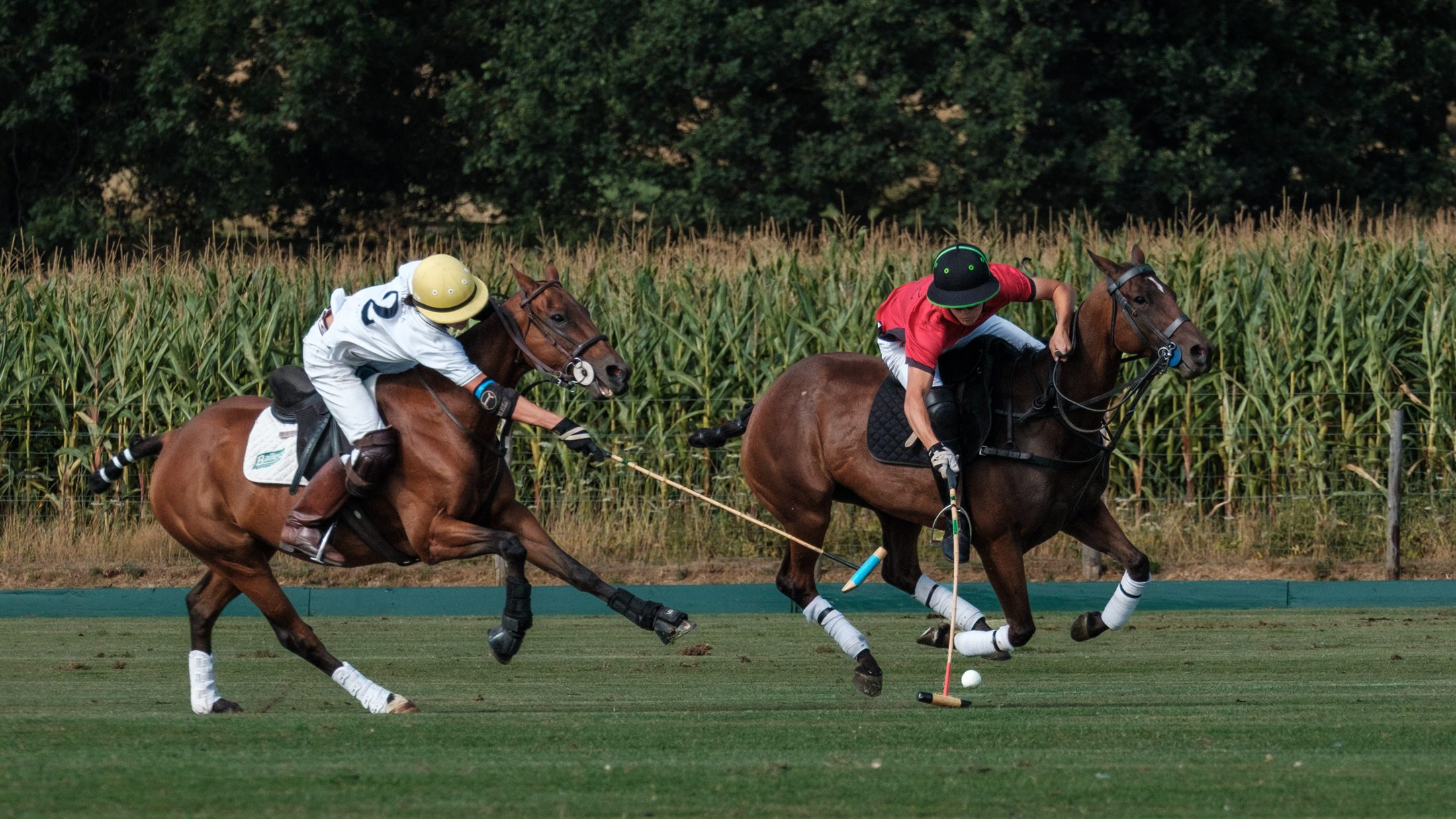 A Mono Polo player in red driving the ball upfield, chased by an opponent, at Lodsworth